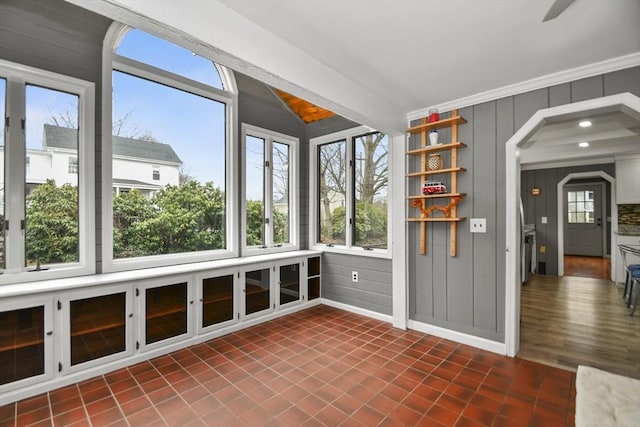 unfurnished sunroom featuring baseboards, arched walkways, vaulted ceiling, and a healthy amount of sunlight