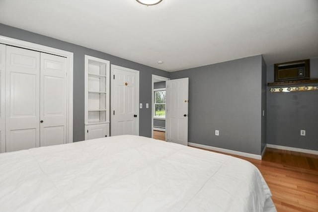 bedroom featuring baseboards, wood finished floors, and a wall mounted air conditioner