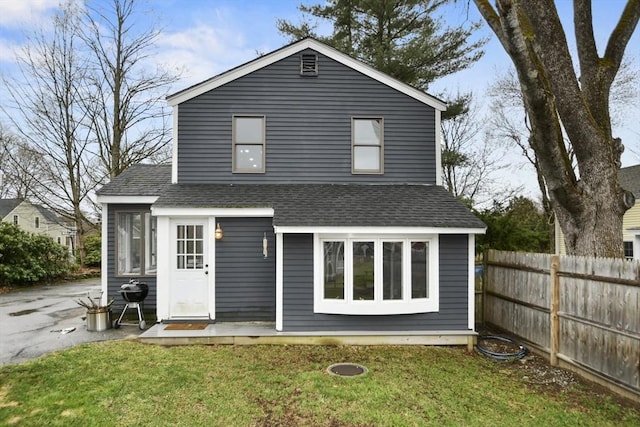 rear view of property with roof with shingles, fence, and a lawn