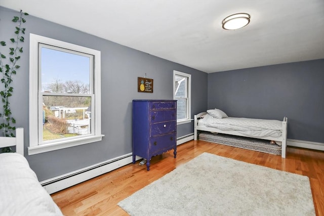 bedroom featuring a baseboard radiator, wood finished floors, and multiple windows