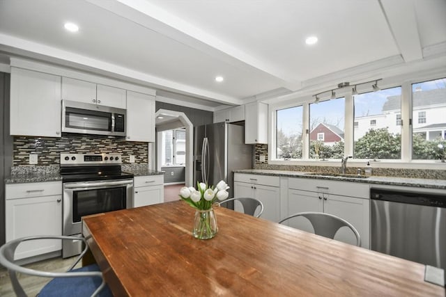 kitchen with white cabinetry, a sink, stainless steel appliances, decorative backsplash, and beam ceiling