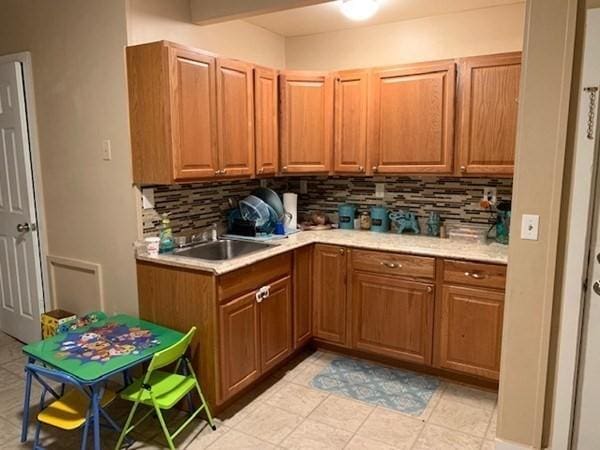 kitchen featuring backsplash, light countertops, brown cabinetry, a sink, and light tile patterned floors