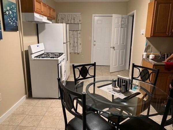 kitchen featuring white range with gas stovetop, under cabinet range hood, baseboards, and brown cabinets