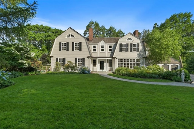 shingle-style home with a front yard, a gambrel roof, and a chimney