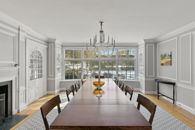 dining space featuring ornamental molding, a chandelier, a fireplace with flush hearth, light wood-style floors, and a decorative wall