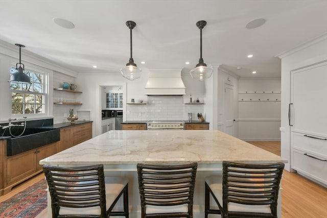 kitchen featuring crown molding, open shelves, stainless steel stove, brown cabinets, and custom range hood