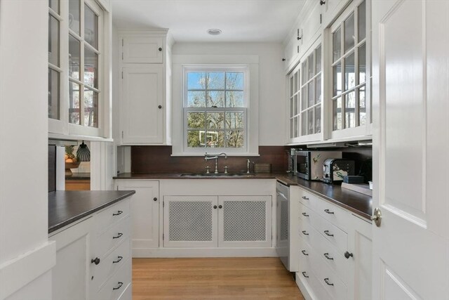 kitchen featuring a sink, light wood-type flooring, dark countertops, and white cabinetry