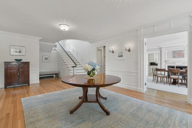 interior space with ornamental molding, light wood-style flooring, a wainscoted wall, stairs, and a decorative wall