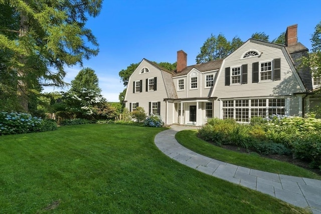 back of house featuring a chimney, a gambrel roof, and a lawn