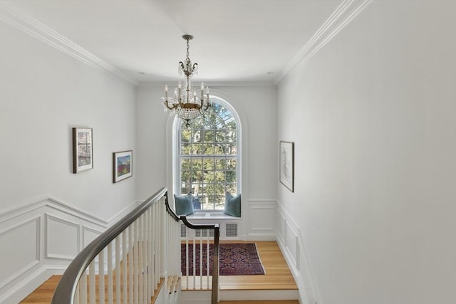 stairway with a decorative wall, an inviting chandelier, wood finished floors, and crown molding