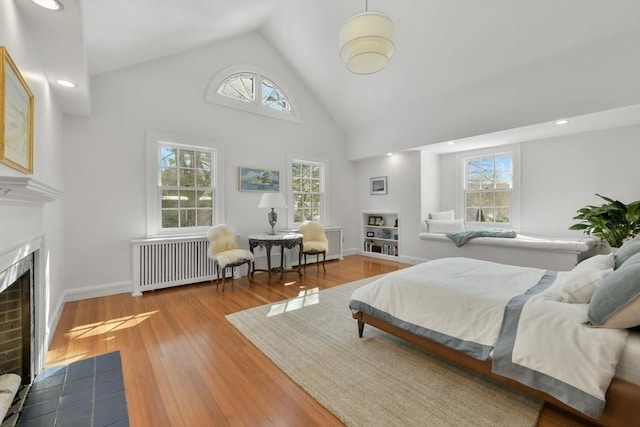 bedroom with high vaulted ceiling, a fireplace with flush hearth, radiator heating unit, baseboards, and hardwood / wood-style flooring