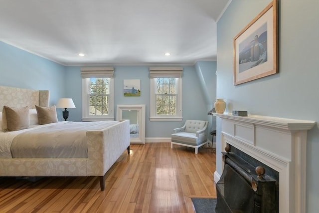 bedroom featuring a fireplace with flush hearth, hardwood / wood-style floors, baseboards, and ornamental molding