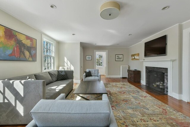 living room featuring radiator heating unit, a tile fireplace, ornamental molding, and wood finished floors