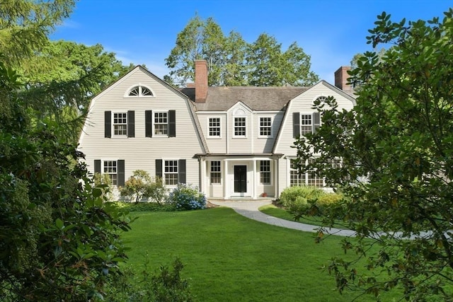view of front of house with a gambrel roof, a front lawn, and a chimney