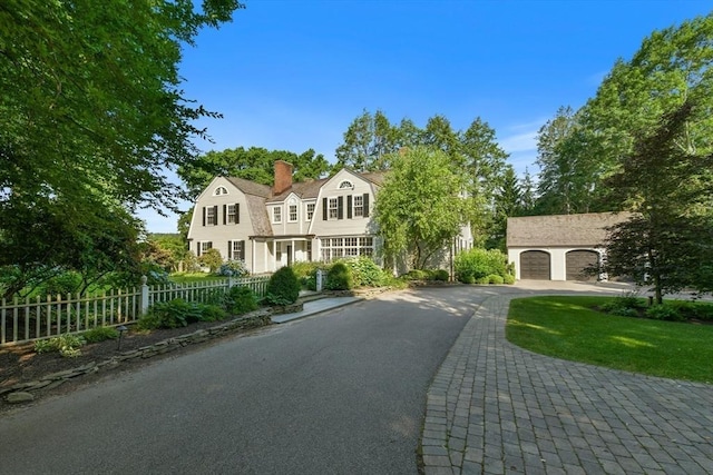 shingle-style home with a garage, a chimney, fence, a gambrel roof, and driveway