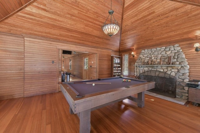 playroom with pool table, a stone fireplace, a high ceiling, wood finished floors, and wooden walls