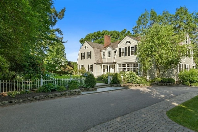 colonial inspired home featuring a gambrel roof, fence, and a chimney