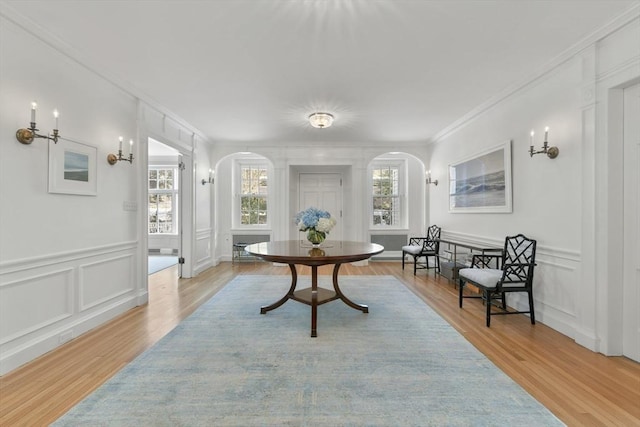 interior space featuring a decorative wall, light wood-style flooring, arched walkways, and crown molding