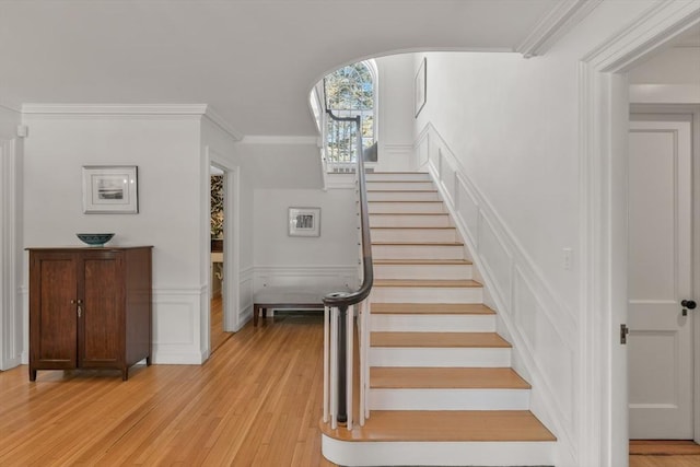 stairway with a decorative wall, ornamental molding, a wainscoted wall, and wood finished floors