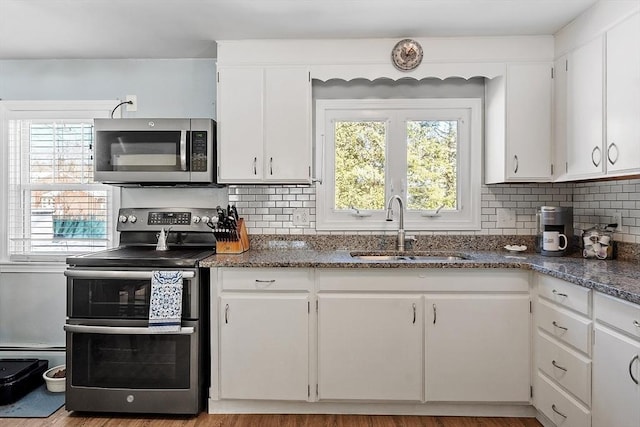 kitchen with a sink, white cabinetry, appliances with stainless steel finishes, dark stone counters, and tasteful backsplash