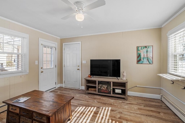 living area featuring light wood finished floors, baseboards, a ceiling fan, a baseboard radiator, and crown molding