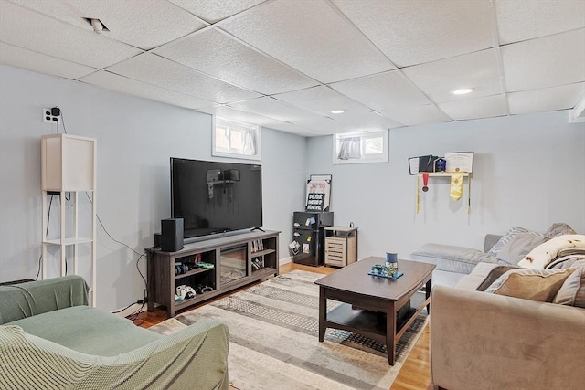 living area with a wealth of natural light, a drop ceiling, and wood finished floors