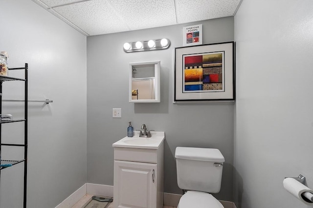 bathroom with a paneled ceiling, baseboards, vanity, and toilet