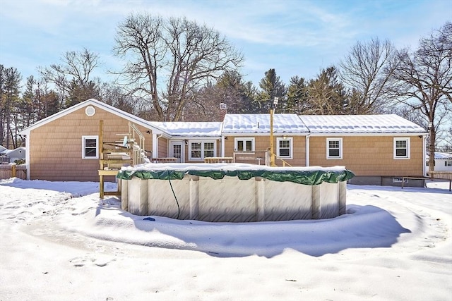 snow covered back of property with a covered pool