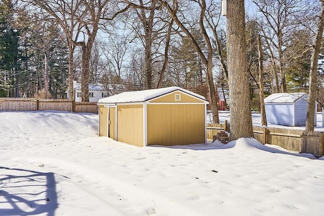 snow covered structure with a storage shed, fence, and an outdoor structure