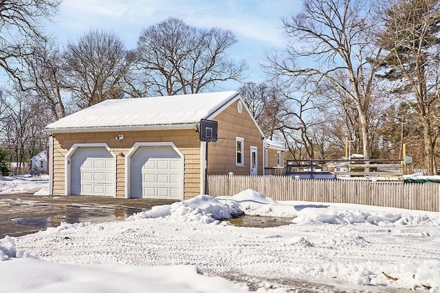 snow covered garage with a garage and fence