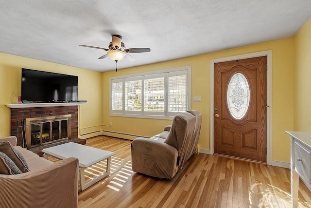 living room featuring light wood-style floors, a baseboard heating unit, a brick fireplace, a ceiling fan, and baseboards