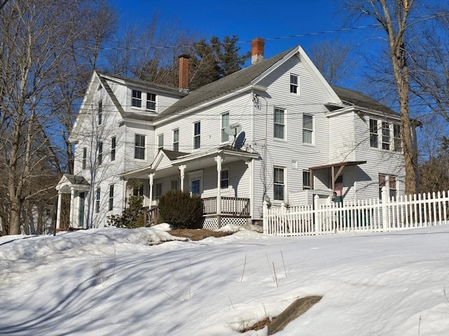 view of front of house with a porch, a chimney, and fence