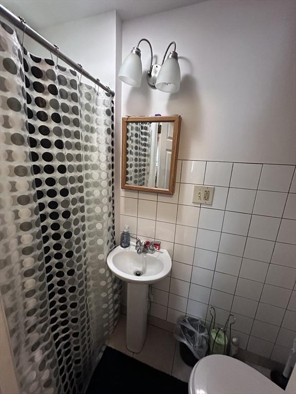 full bathroom featuring toilet, tile walls, curtained shower, and a sink