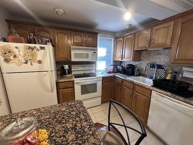 kitchen with white appliances, a sink, tasteful backsplash, light tile patterned floors, and dark countertops