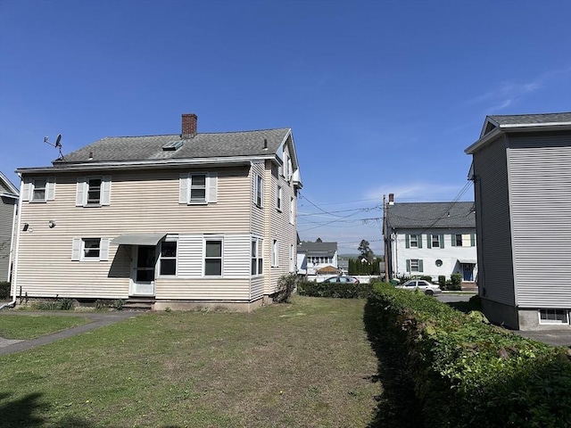 rear view of house featuring entry steps, a chimney, and a yard