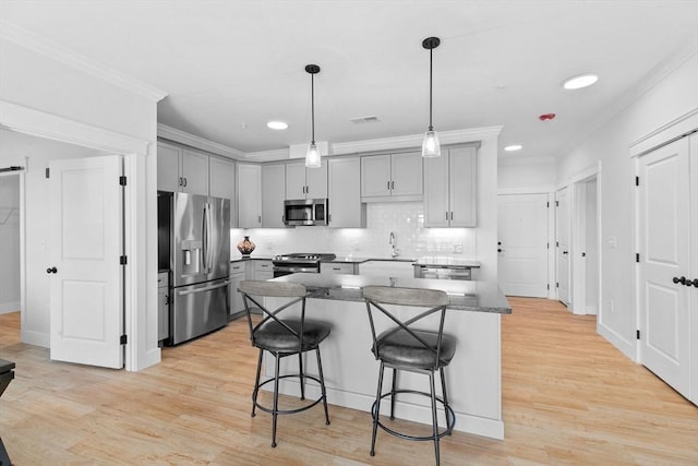 kitchen with decorative backsplash, gray cabinets, a kitchen island, a kitchen bar, and stainless steel appliances