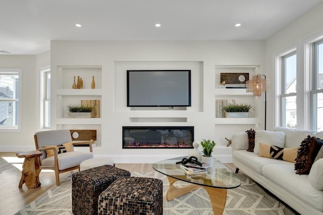 living room with built in features, a glass covered fireplace, recessed lighting, and wood finished floors