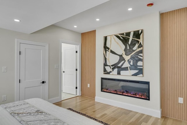 bedroom featuring a glass covered fireplace, baseboards, recessed lighting, and wood finished floors