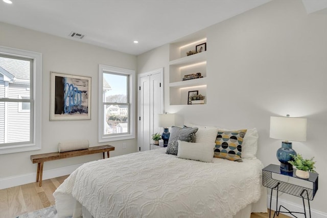 bedroom with multiple windows, visible vents, baseboards, and wood finished floors