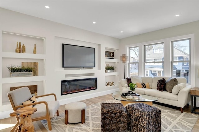 living area with light wood-style floors, recessed lighting, built in shelves, and a glass covered fireplace