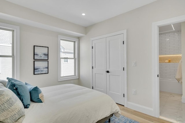 bedroom featuring a closet, multiple windows, ensuite bath, and baseboards