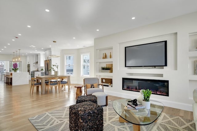 living room with built in features, baseboards, a glass covered fireplace, light wood-style flooring, and recessed lighting