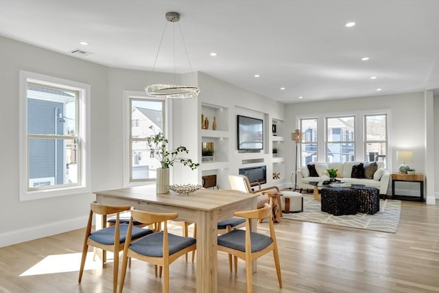 dining area featuring light wood-style flooring, built in features, a wealth of natural light, and a glass covered fireplace