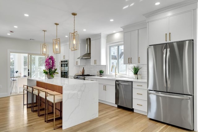 kitchen featuring stainless steel appliances, a sink, wall chimney range hood, a kitchen island, and a kitchen breakfast bar