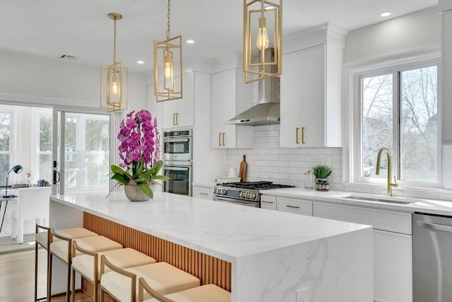 kitchen featuring a center island, stainless steel appliances, tasteful backsplash, a sink, and wall chimney range hood