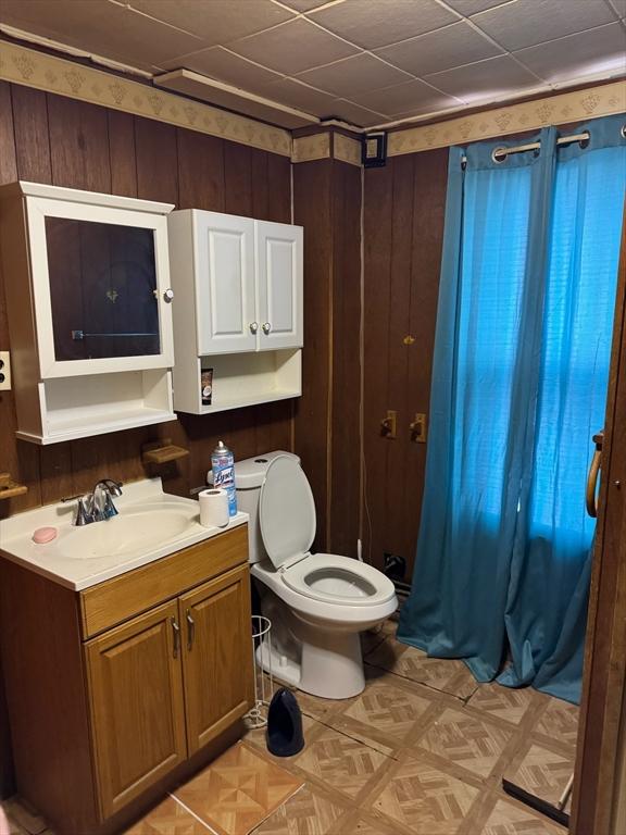 bathroom with toilet, parquet flooring, vanity, and wooden walls