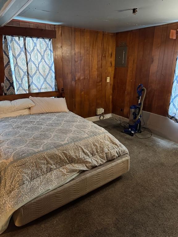 carpeted bedroom featuring electric panel and wood walls