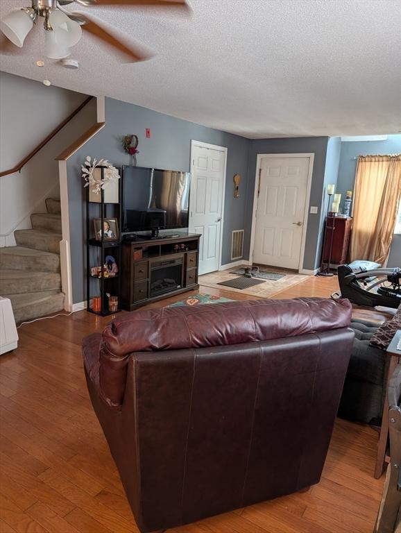 living room with wood-type flooring, ceiling fan, and a textured ceiling