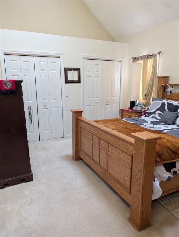 carpeted bedroom with high vaulted ceiling and two closets