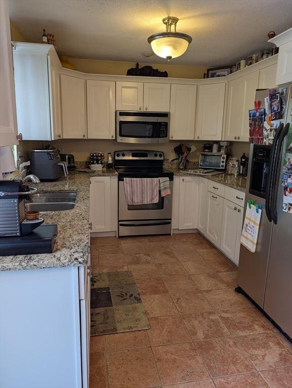 kitchen featuring stainless steel appliances, light stone countertops, white cabinets, and a textured ceiling